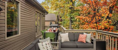 A covered outdoor seating area with a sofa and chairs, a dining table with chairs, and a grill.