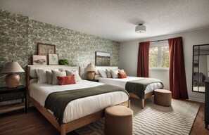 A bedroom with two beds, a large window with red curtains, a mirror, and a textured wall.