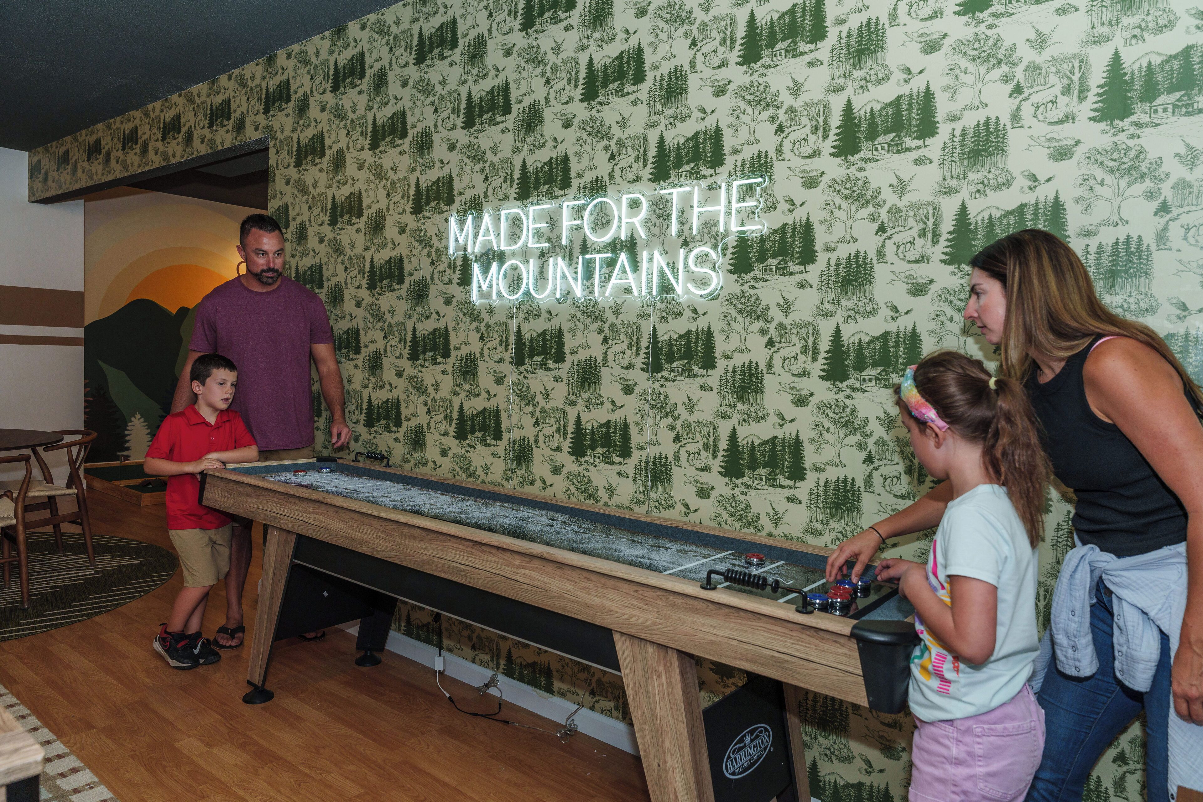 Ein Zimmer mit einem Holztisch, einem Neon-Schild mit der Aufschrift 'MADE FOR THE MOUNTAINS' und dekorativer Tapete.