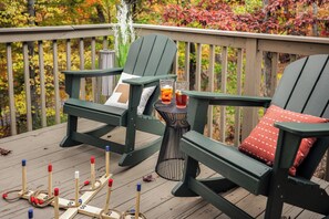 Eine Terrasse mit zwei grünen Adirondack-Stühlen, einem kleinen runden Tisch mit Getränken und einer Croquet-Ausrüstung.