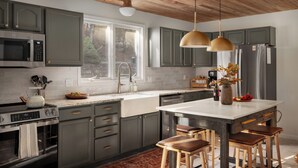 A modern kitchen with grey cabinets, a large island with stools, a built-in oven, and a window providing natural light.