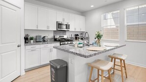 A modern kitchen with white cabinets, a granite countertop, a stainless steel microwave, and a large island with stools.