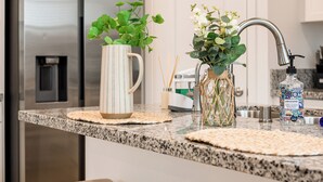 A kitchen with white cabinets, a stainless steel refrigerator, a granite countertop, and two stools.