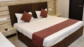 A neatly made bed with a white and brown bedspread, two pillows, and a wooden headboard. - Hotel Naman Palace (Varanasi)