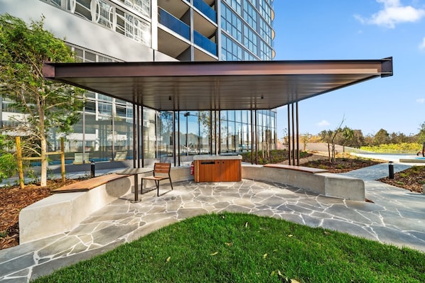 A modern outdoor seating area with a stone floor, a wooden bench, and a glass enclosure.