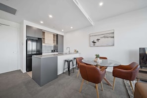 A modern kitchen with a built-in island, a dining area with a glass table and leather chairs, and a painting on the wall.