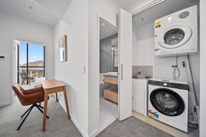 Un appartement moderne comprenant un coin repas, une vue dégagée sur l’extérieur grâce à une porte ouverte, un lave-linge et une petite cuisine.