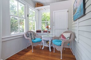 A sunlit room with white walls, a wooden floor, wicker chairs with blue cushions, a small round table, and a door.