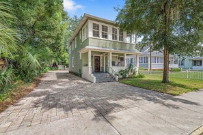 A two-story house with a front porch, a brick driveway, and a well-maintained lawn.