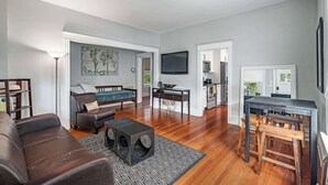 A spacious living area with a sofa, coffee table, and a TV. There is a kitchen area with a microwave and a dining table. - Old City Charm l Historic l Walk to St George (St. Augustine)