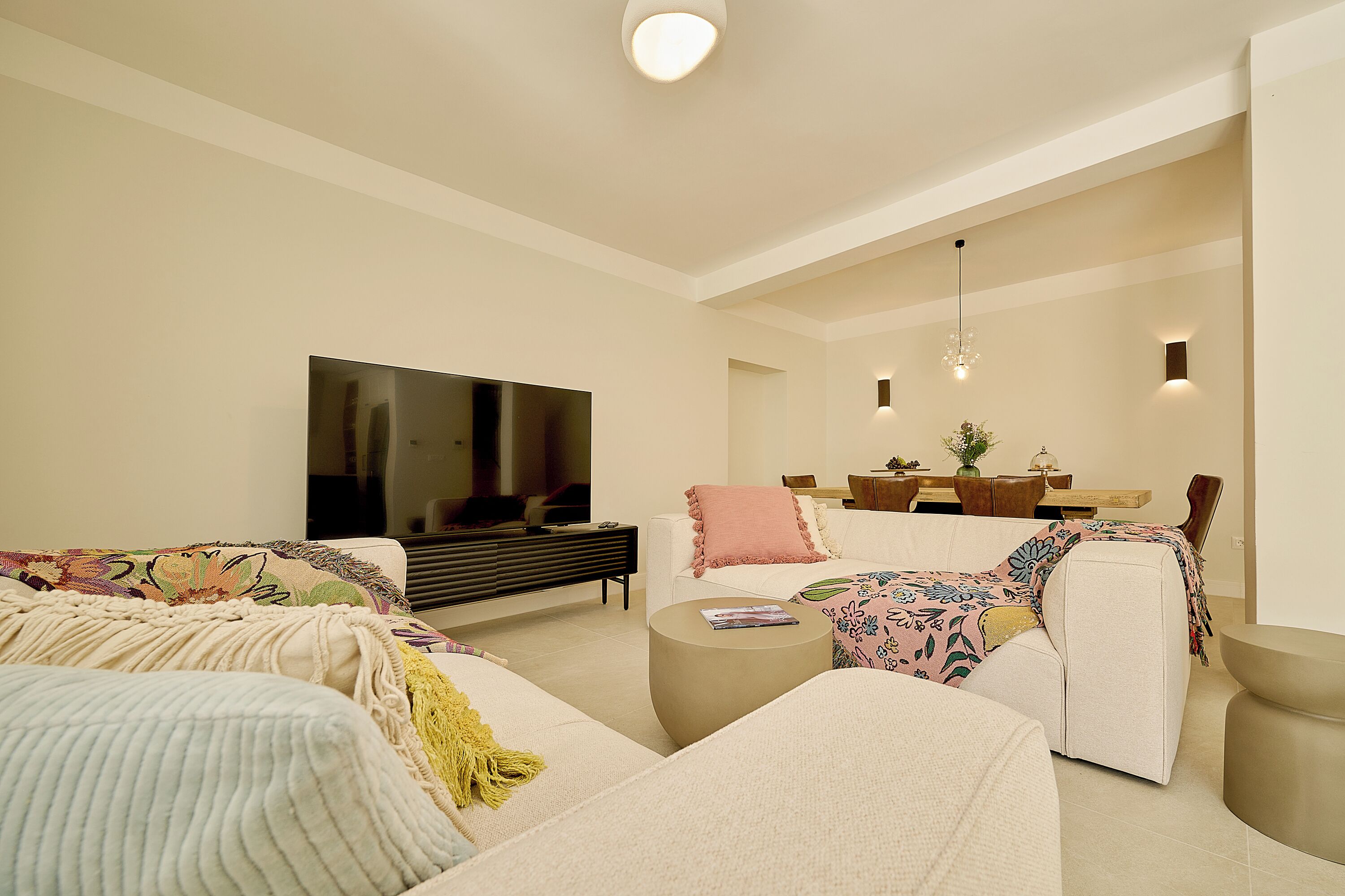 A modern living room with a flat-screen TV, sofas, a coffee table, and a dining area with a wooden table and chairs.