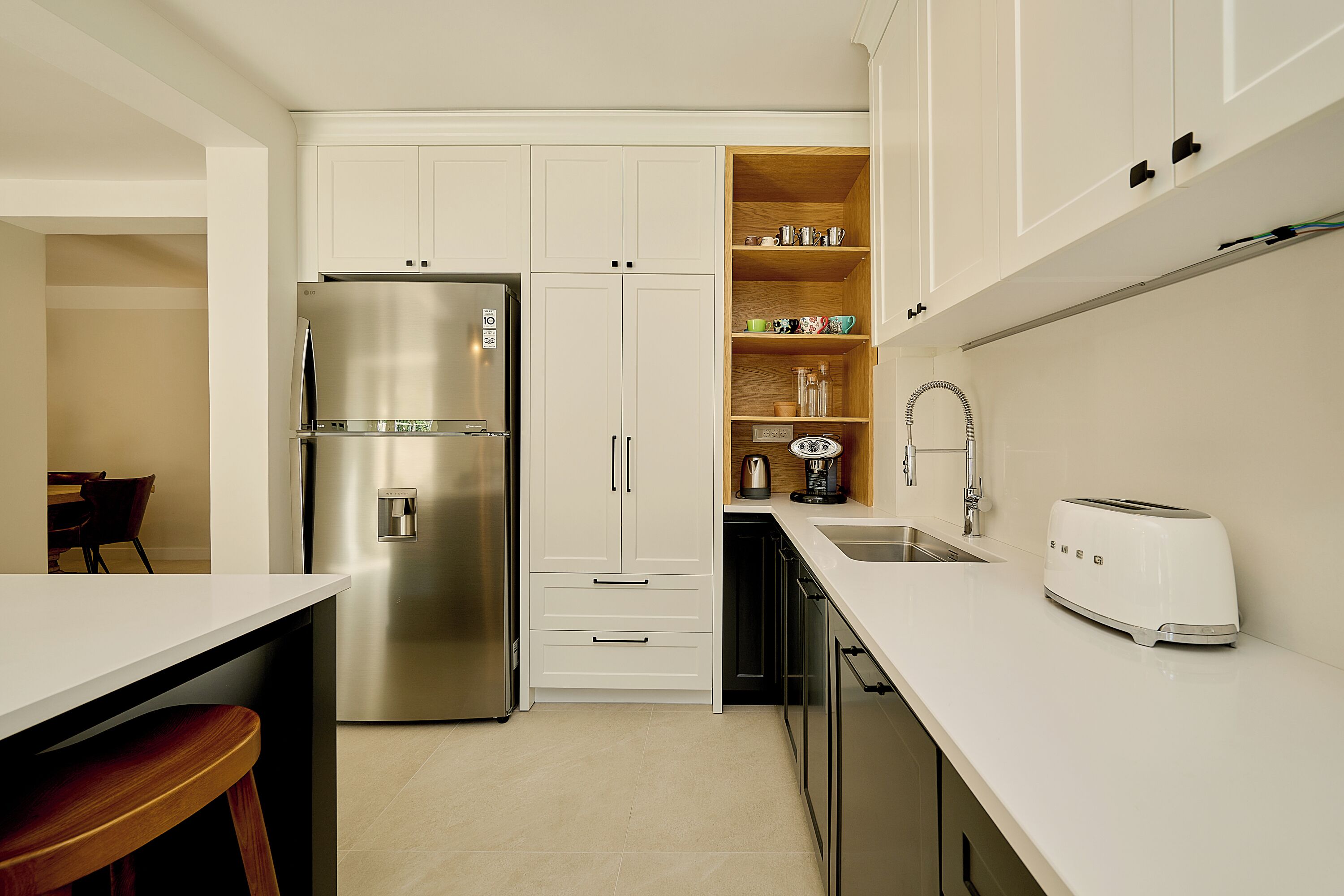 A modern kitchen with white cabinetry, a stainless steel refrigerator, a built-in oven, a sink, and a toaster.