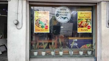 Un escaparate con un letrero que dice 'MVM Transient House' y dos carteles publicitando 'Kare Kare & Bulalo House' y 'Kare Kare Crujiente'.