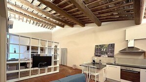 A compact living space with a TV, white shelving unit, a dining area with chairs, and a kitchen with a stove and sink.