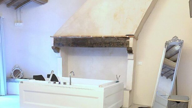 A modern bathroom with a freestanding bathtub, a large mirror, and two sun loungers.
