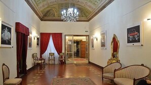A lobby with a chandelier, red curtains, and framed artwork on the walls.