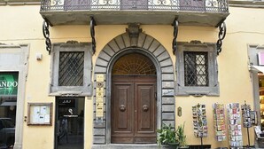 A building with a large wooden door, two windows with metal grilles, and a balcony with decorative ironwork.