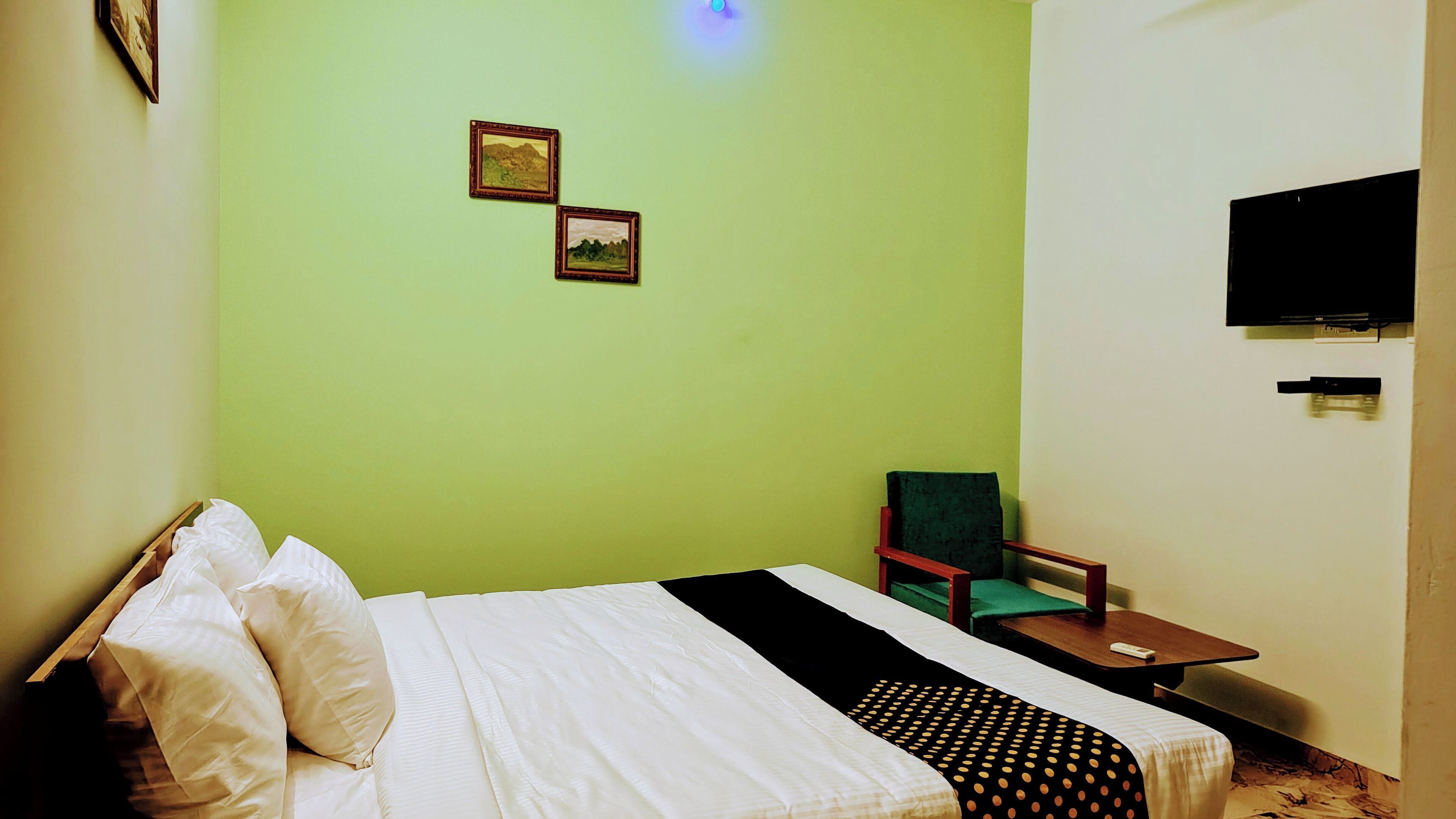 A room with a bed, a chair, a small table, and a flat-screen TV mounted on the wall.