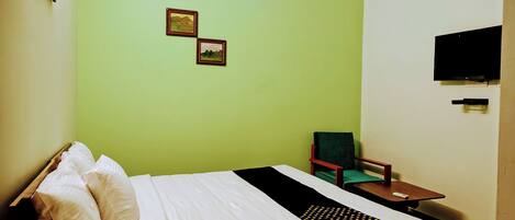 A room with a bed, a chair, a small table, and a flat-screen TV mounted on the wall.
