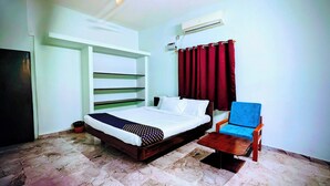 A bedroom with a bed, a chair, a small table, a wall-mounted air conditioner, and a red curtain.