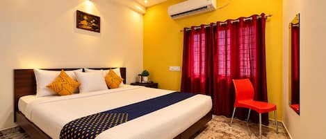 A hotel room with a bed, a red chair, a ceiling fan, an air conditioning unit, and a small plant on the nightstand.
