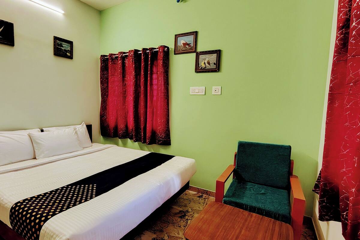 A bedroom with a bed, a chair, and a window with red curtains.