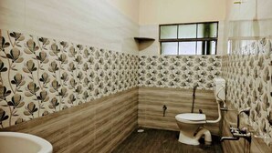 A bathroom with a toilet, sink, and shower area. The walls have a leaf pattern wallpaper.