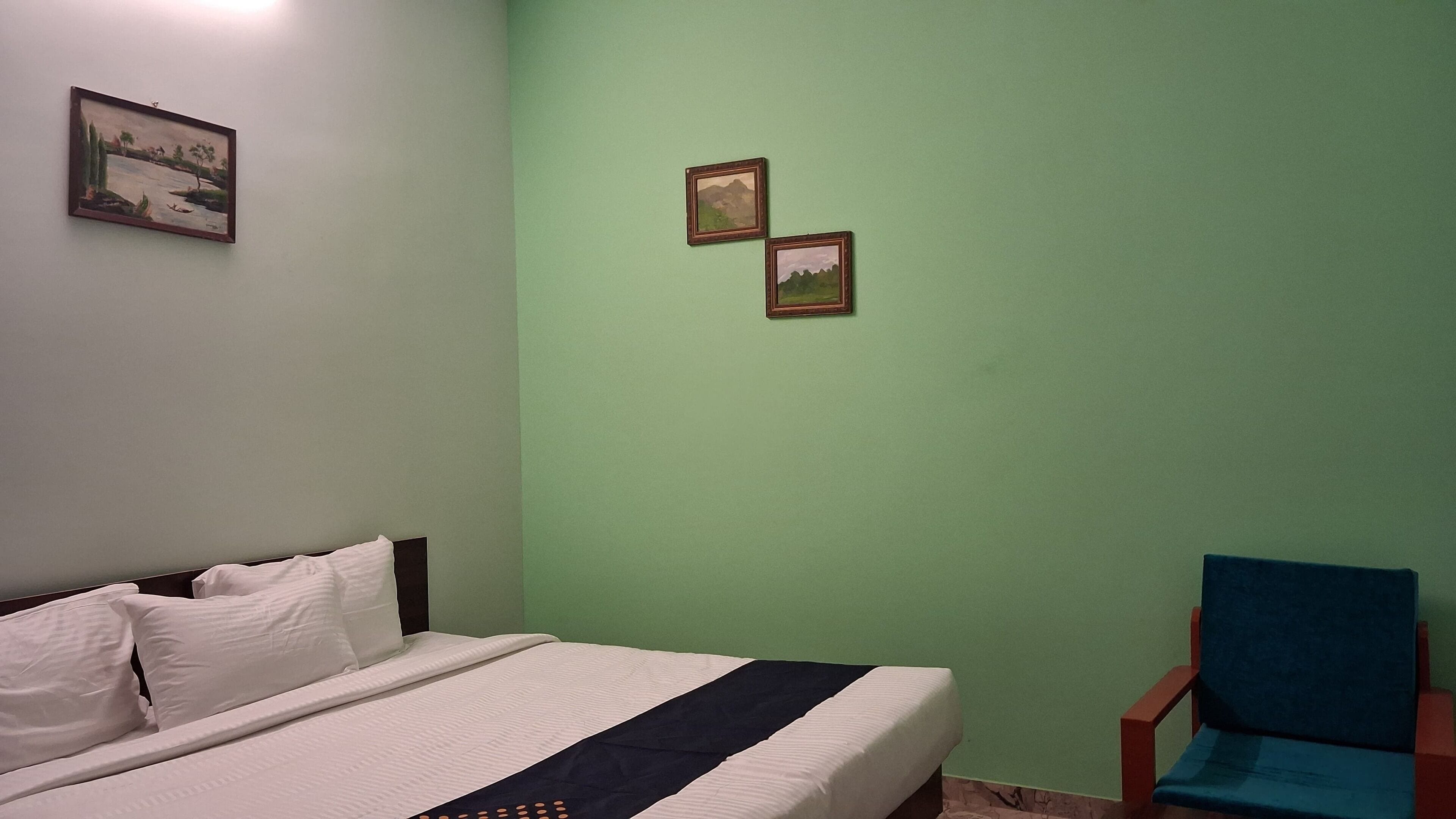 Un dormitorio con una cama, una silla y dos cuadros en la pared.