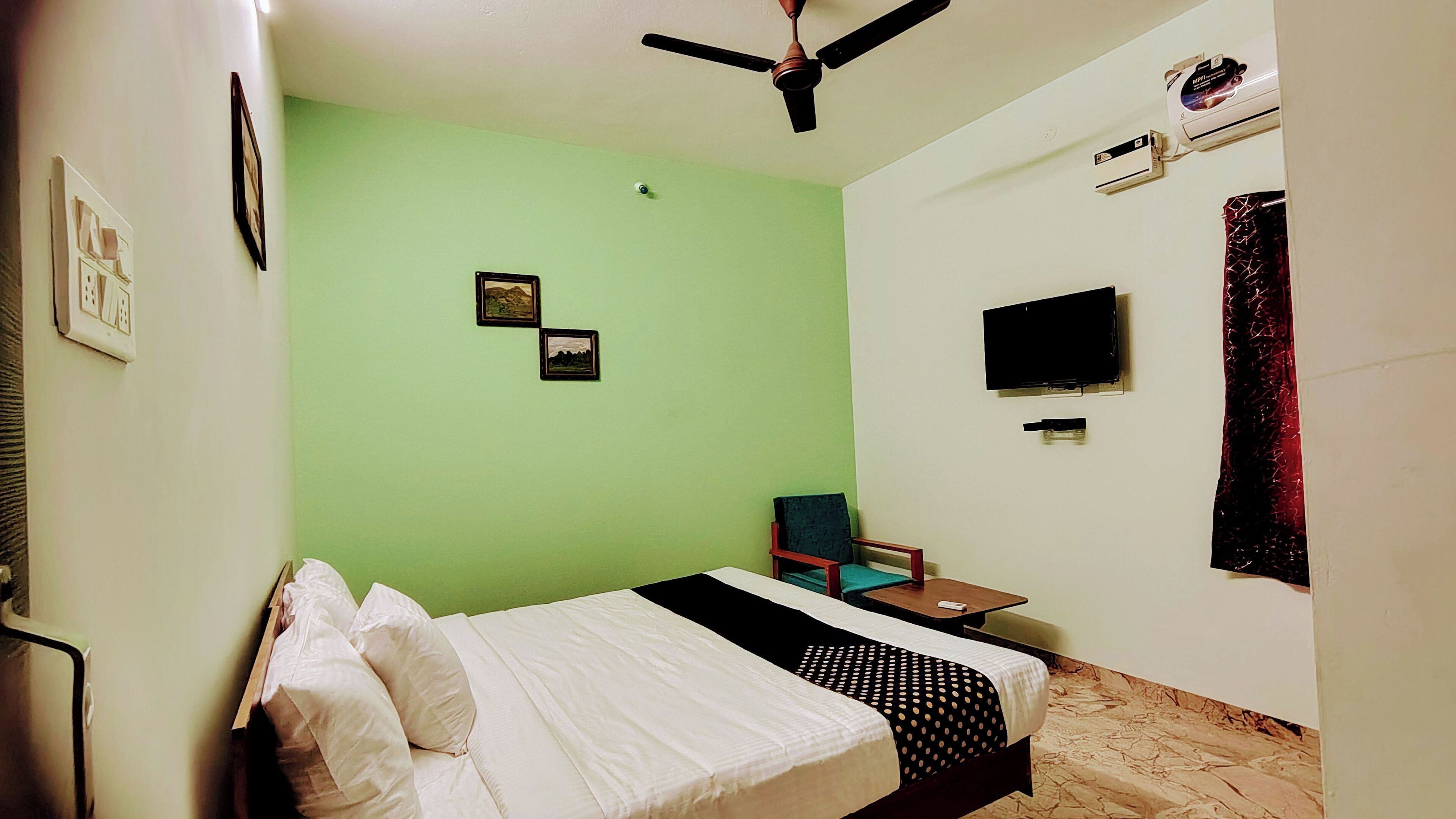 A bedroom with a bed, a chair, a television, and an air conditioning unit.