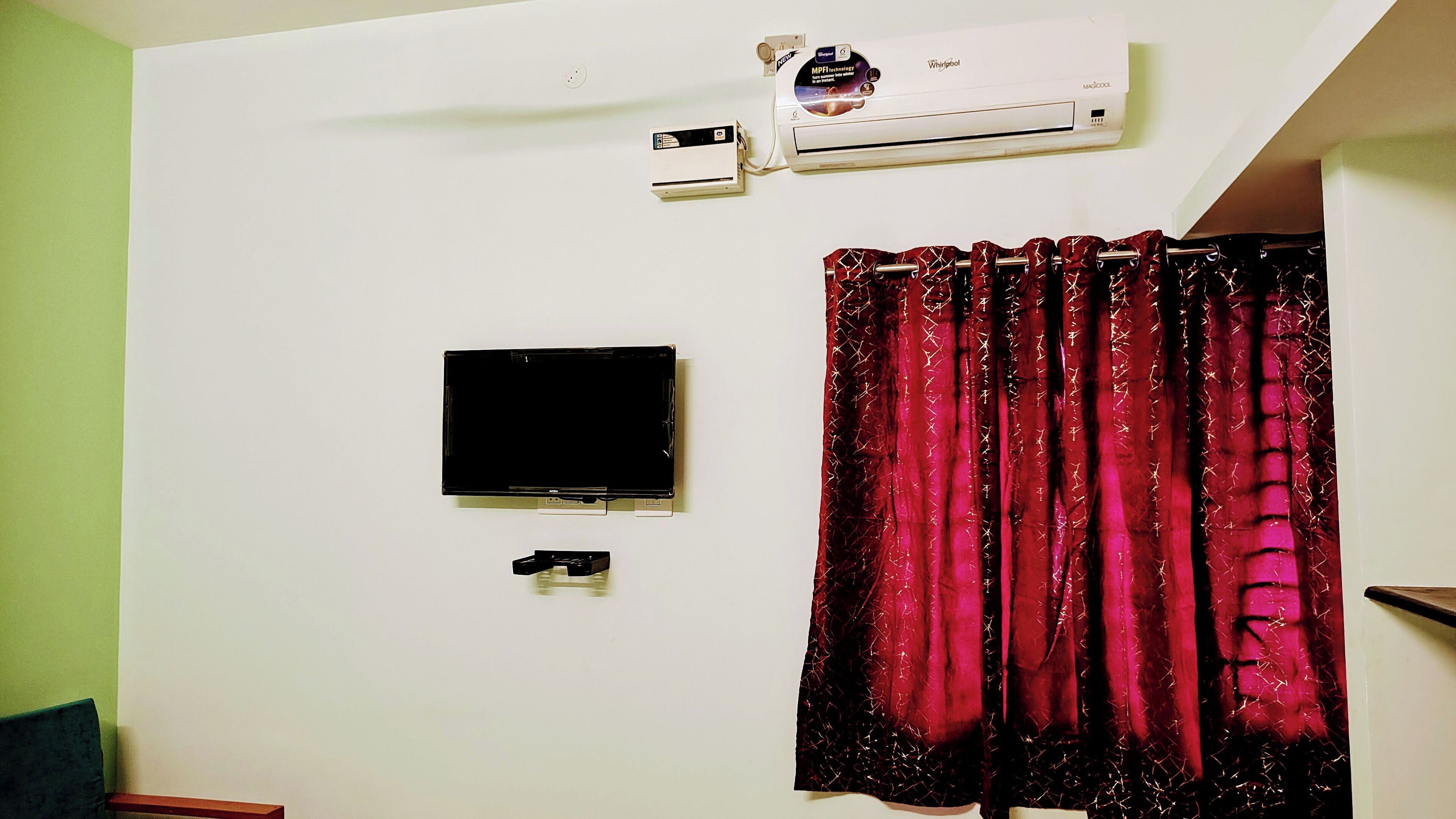 A room with a mounted air conditioner, a flat-screen TV, and a curtain.