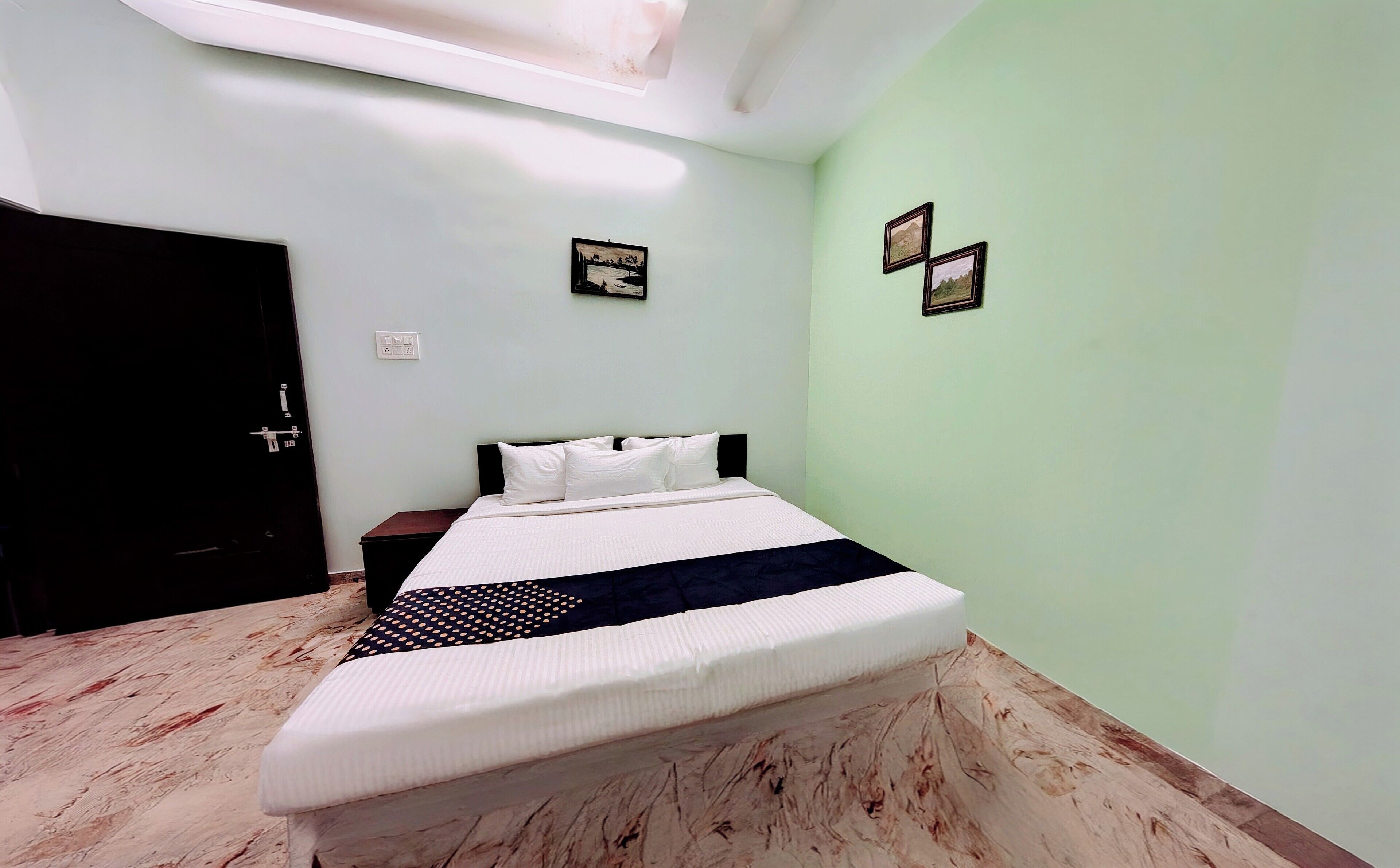 A bedroom with a bed, a nightstand, a door, and a light switch on the wall.