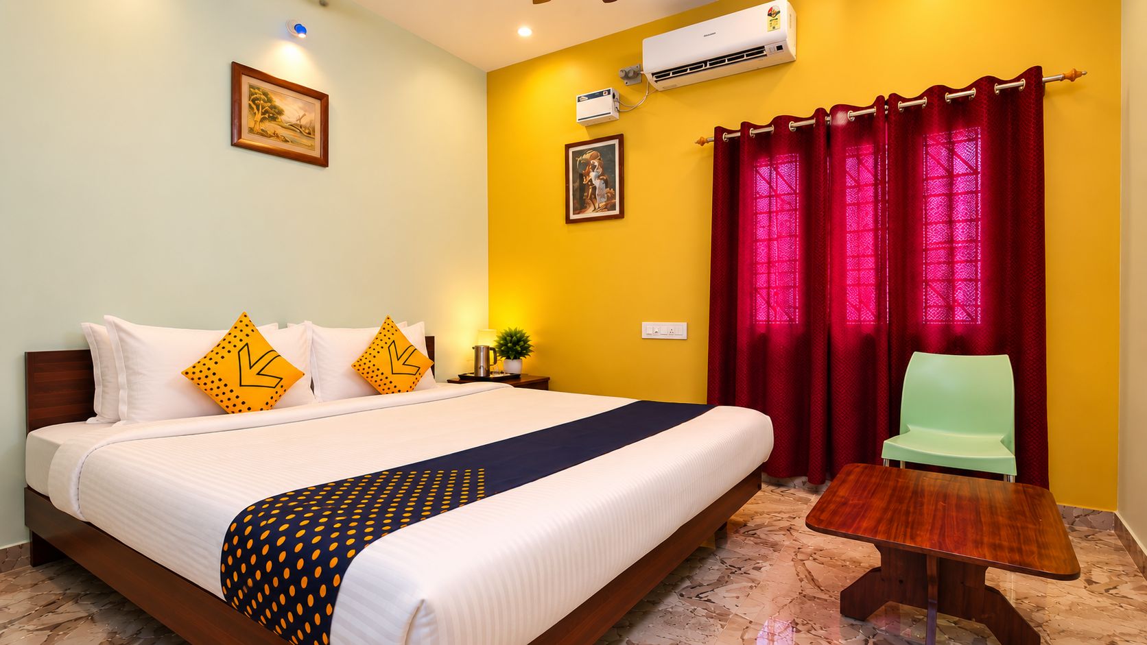 A hotel room with a bed, a chair, a table, an air conditioner, and curtains.