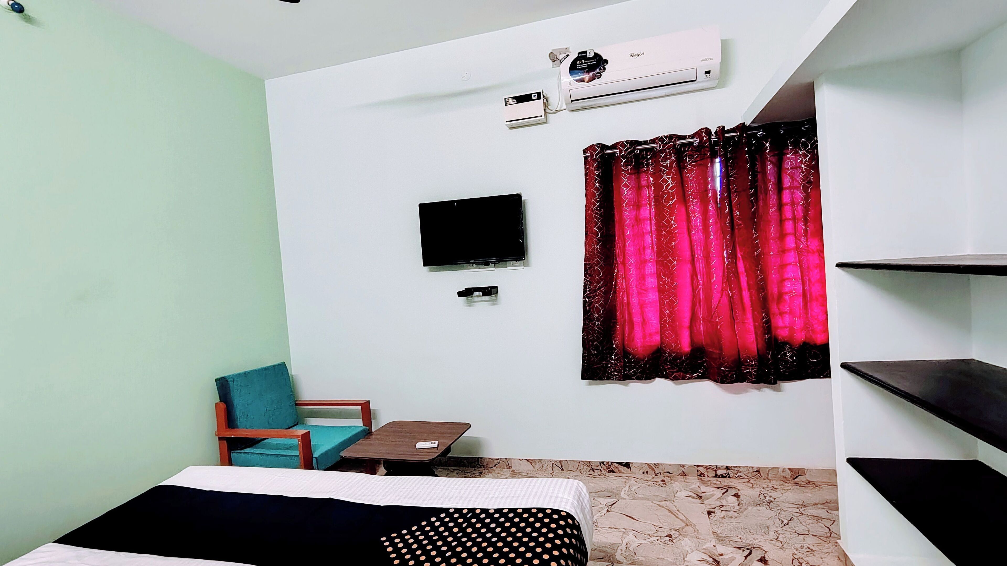 A bedroom with a bed, a TV, an air conditioner, a chair, and a shelf.