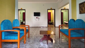 A hotel lobby with a marble floor, blue upholstered chairs, a wooden table, and a flat-screen TV mounted on the wall.