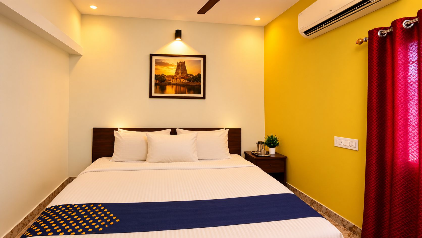 Habitación de hotel con cama, mesita de noche, aire acondicionado montado en la pared y un cuadro enmarcado sobre la cama.