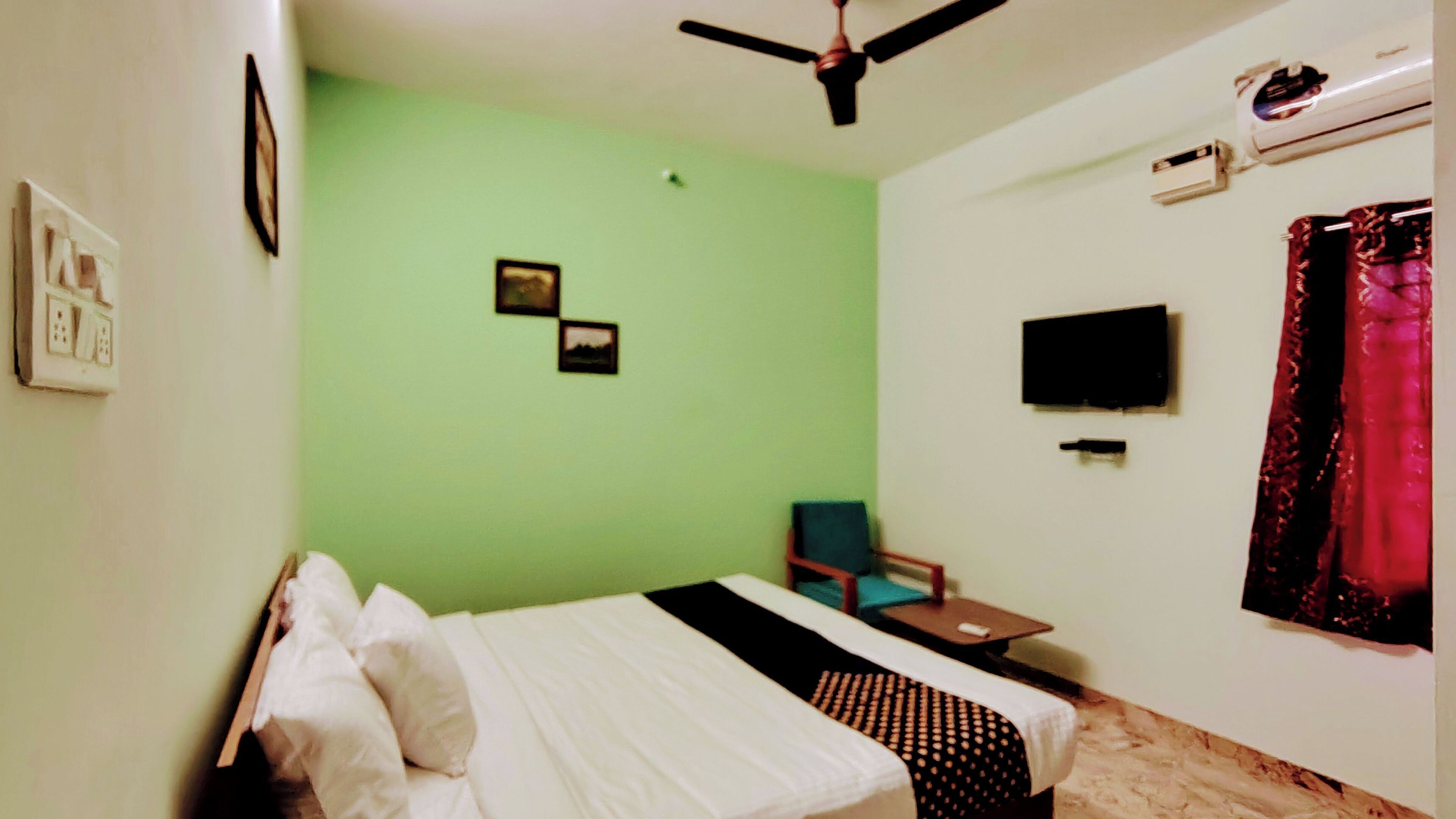 Una habitación con cama, ventilador de techo, televisión y ventana con cortinas.
