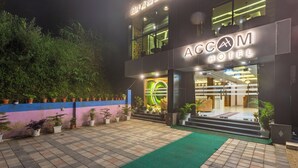 Exterior del HOTEL ACCOM con una entrada bien iluminada, un felpudo verde y plantas en macetas a lo largo del camino.