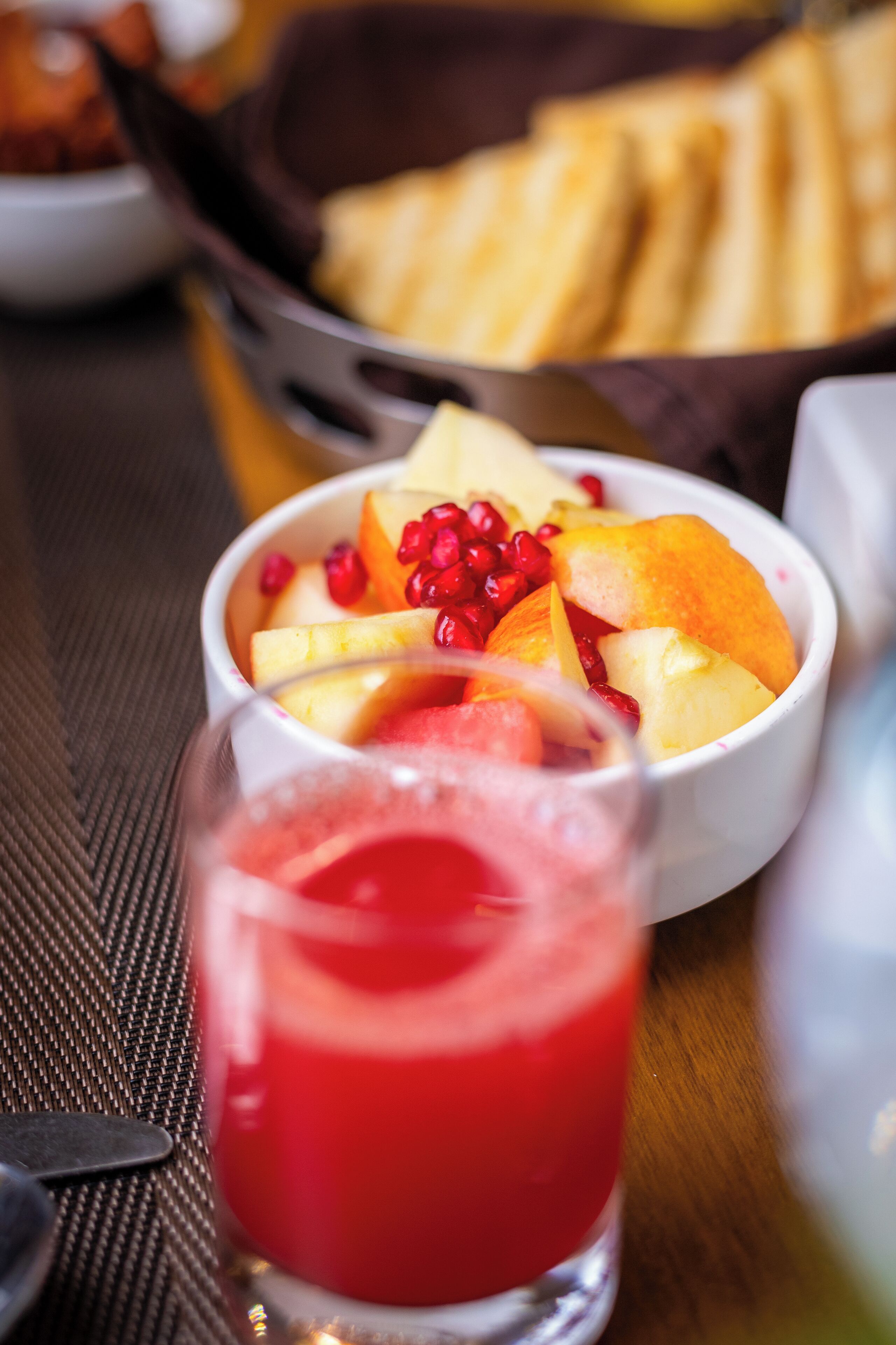 A bowl of fruit and a glass of red drink on a table.