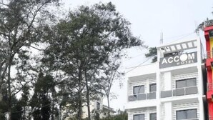 A modern building with a sign for ACCOM HOTEL, featuring a gated entrance and a paved driveway.