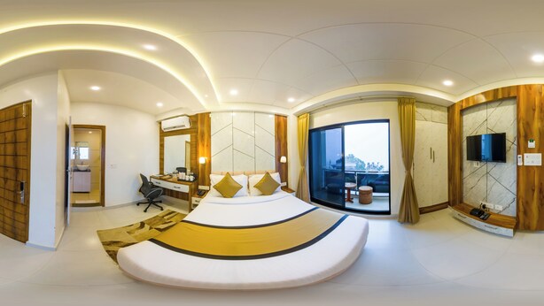 Un dormitorio moderno con una cama curvada, un escritorio, una silla, un televisor y un balcón con vistas.