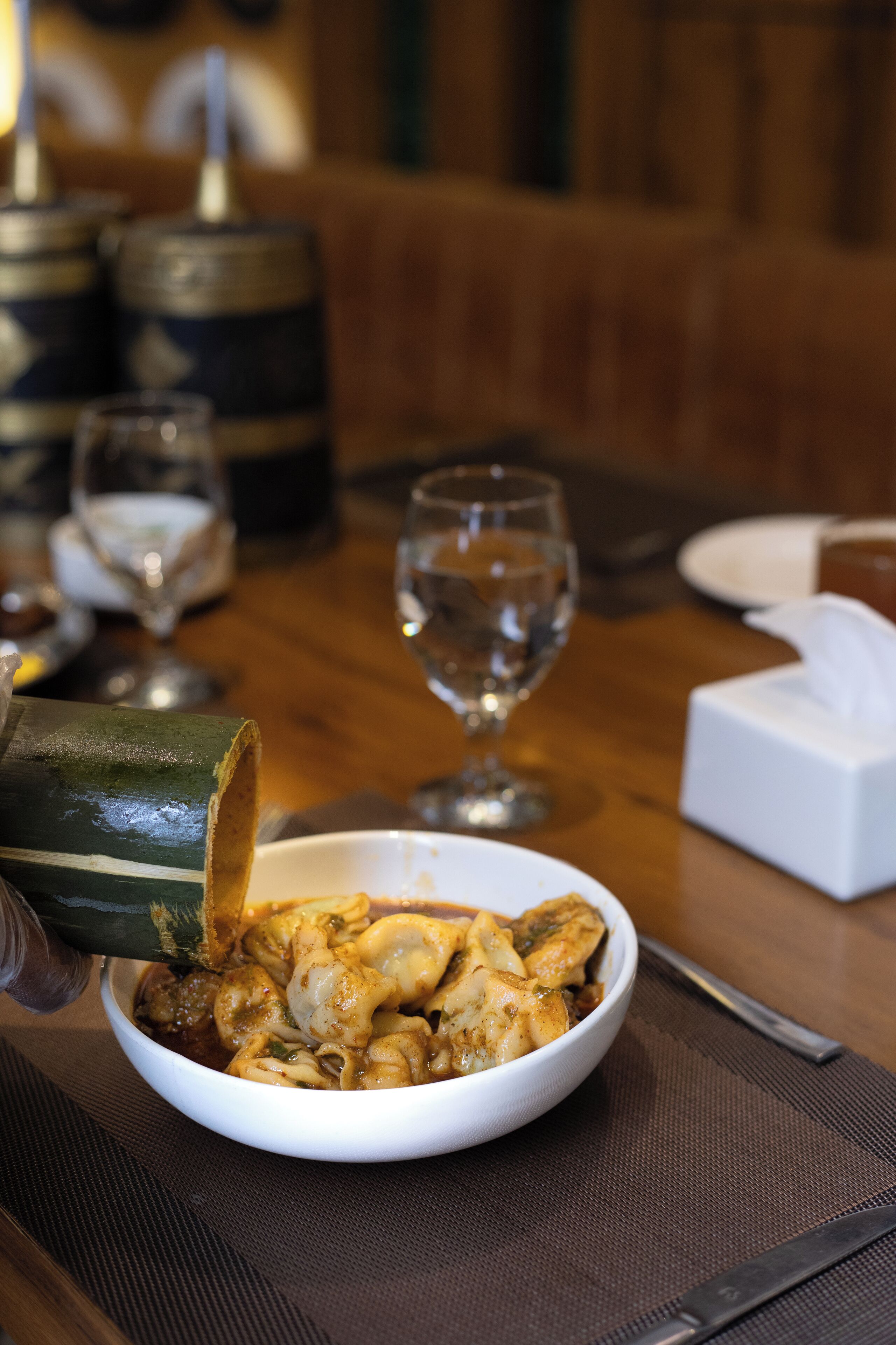 A dining table with a bowl of food, a wine glass, and a bottle.