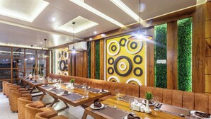 Un restaurante moderno con largas mesas de madera, cabinas acolchadas y una pared vertical con jardín.