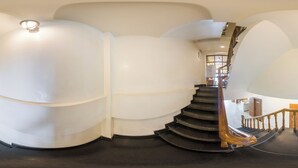 Una escalera de caracol con barandillas de madera y piso negro, rodeada de paredes blancas y un aplique de techo.