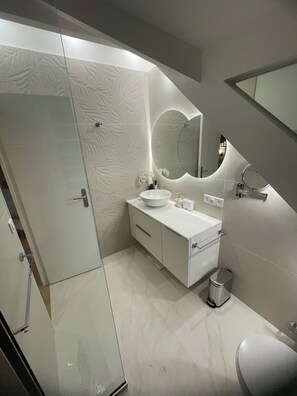 Ein modernes Badezimmer mit einem weißen Waschtisch, einem großen Spiegel und einer Duschkabine aus Glas.