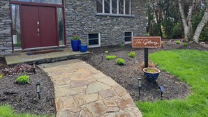 Una casa de piedra con una puerta roja, un cartel que dice "The Getaway 670 Shultz Rd", y un camino de piedra que conduce a la entrada.