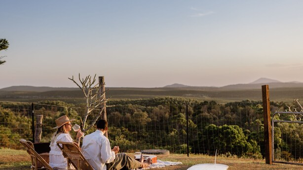 A couple and a child relaxing on a wicker chair with a view of a mountainous landscape. - Salt Shack - Classic Angourie Beach Cottage Steps from Spooky Beach - Holiday Yamba (Angourie)
