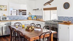A modern kitchen with white cabinets, a wooden dining table, and a stove. - Salt Shack - Classic Angourie Beach Cottage Steps from Spooky Beach - Holiday Yamba (Angourie)