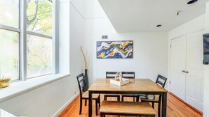 A dining room with a wooden table and chairs, a vase with branches, and a painting on the wall. - Modern 3BR Townhouse with Private Rooftop & Parking Minutes to NYC (Hoboken)