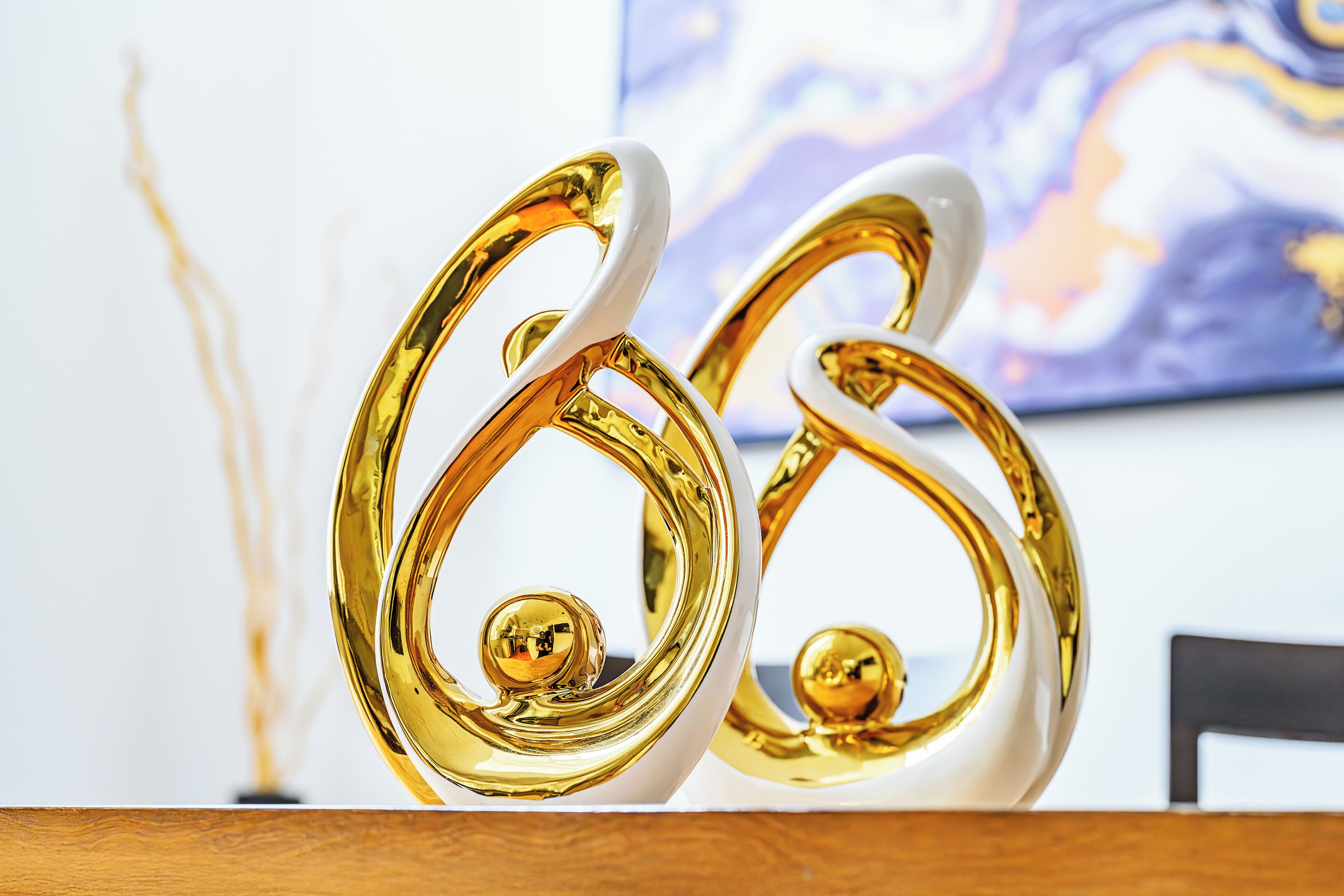 Two golden, white, abstract sculptures on a wooden surface.