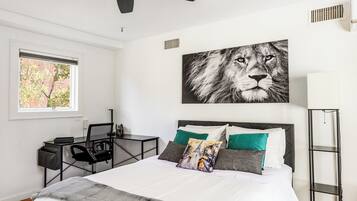A bedroom with a bed, a desk, a chair, a standing lamp, and a ceiling fan.